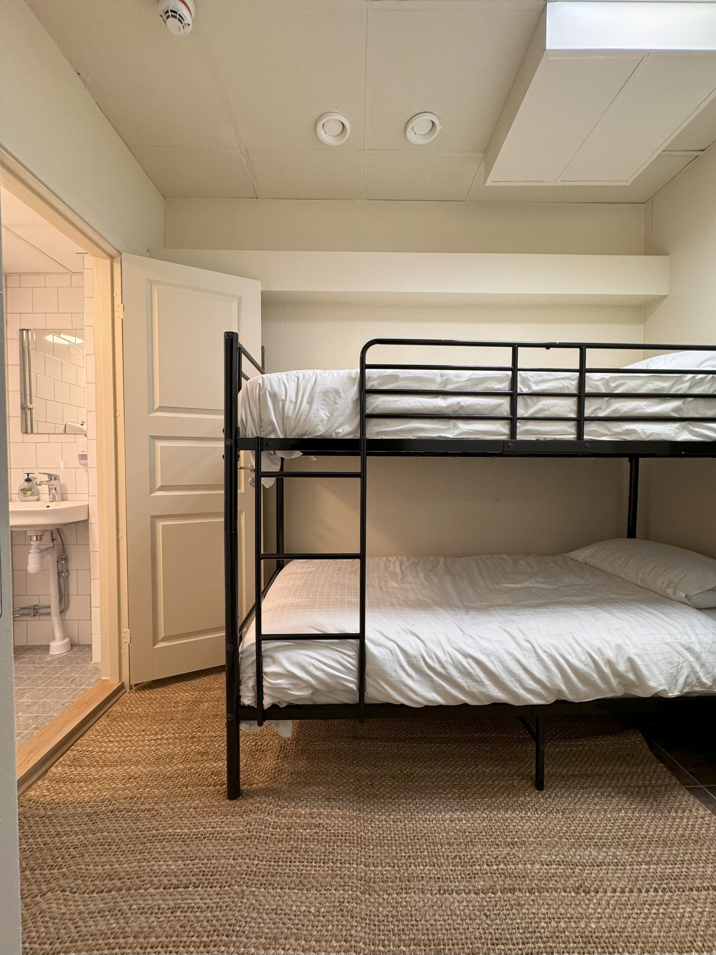 A bunk bed room with a white door, a small sink, and a ceiling light.