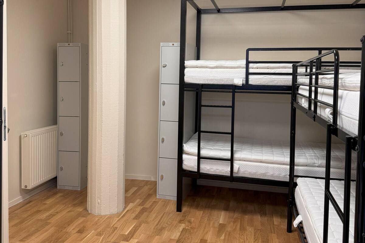 Une chambre avec un lit superposé, un radiateur, une armoire et une bouche d’aération au plafond.