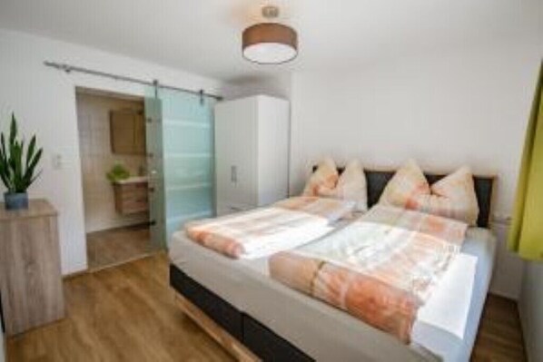 Une chambre moderne avec un lit, une cabine de douche en verre et un plancher en bois.