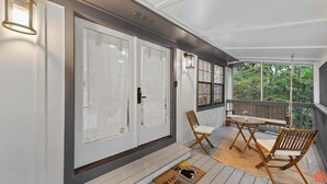 A covered porch with a wooden table and chairs, a sliding glass door, and a view of trees through the windows. - Beach Treehouse Natures Hideaway Close to 30A (Santa Rosa Beach)