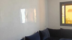 Una stanza con un divano blu scuro, una finestra con vista su un edificio e un condizionatore d'aria bianco a parete.
