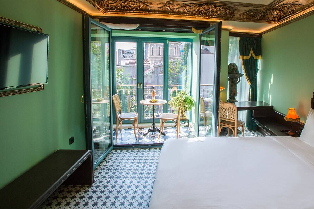 A hotel room with a bed, a desk, a chair, a small table, and a view of the outside.