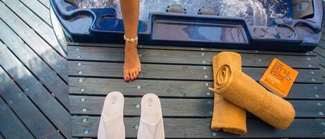 A wooden deck with a hot tub, a pair of white flip-flops, and a rolled-up towel with a book titled "The Subtle Art of Not Giving a F*ck" by Mark Manson.