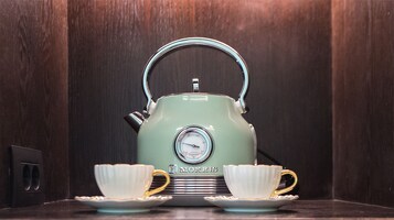 Ein alter Morris-Teekessel mit Temperaturanzeige, zwei dazu passende Tassen und ein Untertasse auf einer Holzoberfläche.