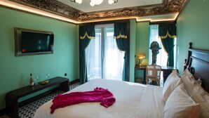 A hotel room with a large bed, a flat-screen TV mounted on the wall, a desk with a lamp, and a chair. - Juan Rodriguez Hacienda (Athens)