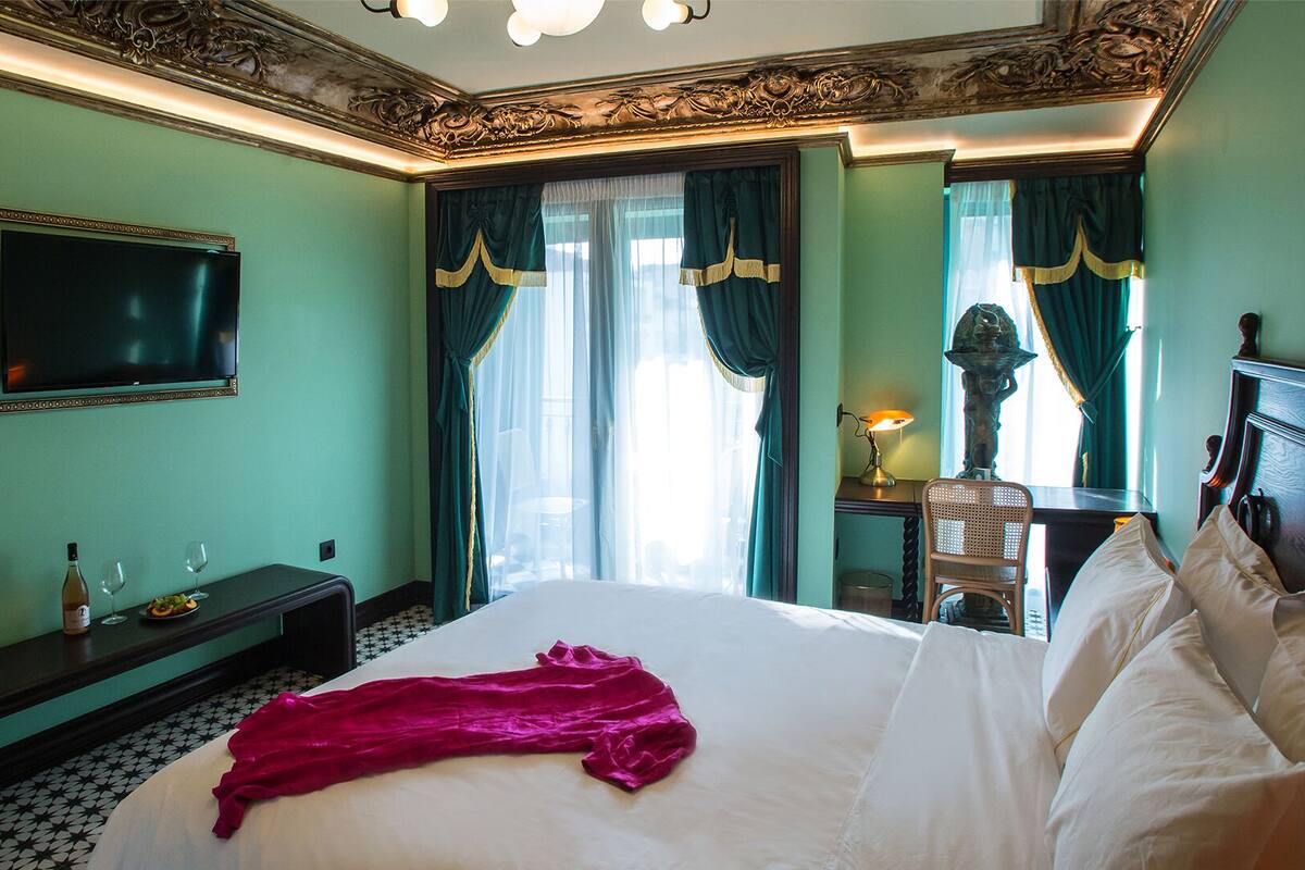 A hotel room with a large bed, a flat-screen TV mounted on the wall, a desk with a lamp, and a chair.