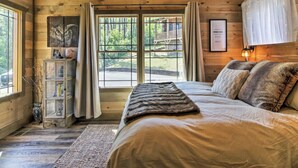 A cozy bedroom with a large bed, wooden walls, and a view of the outdoors. - Newly Listed Cabin w/ Game Room, Hot Tub & Theater (Sevierville)