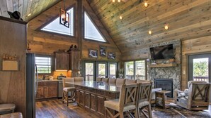 A spacious living area with a large wooden ceiling, a stone fireplace, and a bar area with stools. - Newly Listed Cabin w/ Game Room, Hot Tub & Theater (Sevierville)