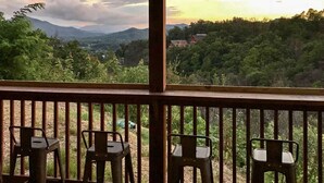 A wooden deck with four chairs facing a scenic view of a forested valley and mountains during sunset. - Newly Listed Cabin w/ Game Room, Hot Tub & Theater (Sevierville)