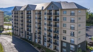 A multi-story residential building with balconies, a parking lot, and a view of the surrounding landscape.