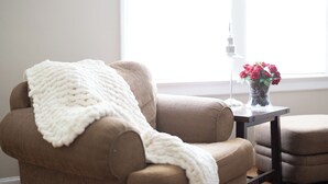 A brown sofa with a white knitted blanket, a small table with a vase of red flowers, and a window with natural light. - Lovely Historic District Retreat (Columbus)