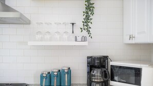 A kitchen with white tiled walls, a white cabinet, a coffee maker, a microwave, and three teal containers. - Lovely Historic District Retreat (Columbus)