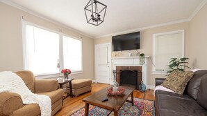 A living room with a brown couch, a coffee table, a fireplace, and a television mounted on the wall. - Lovely Historic District Retreat (Columbus)