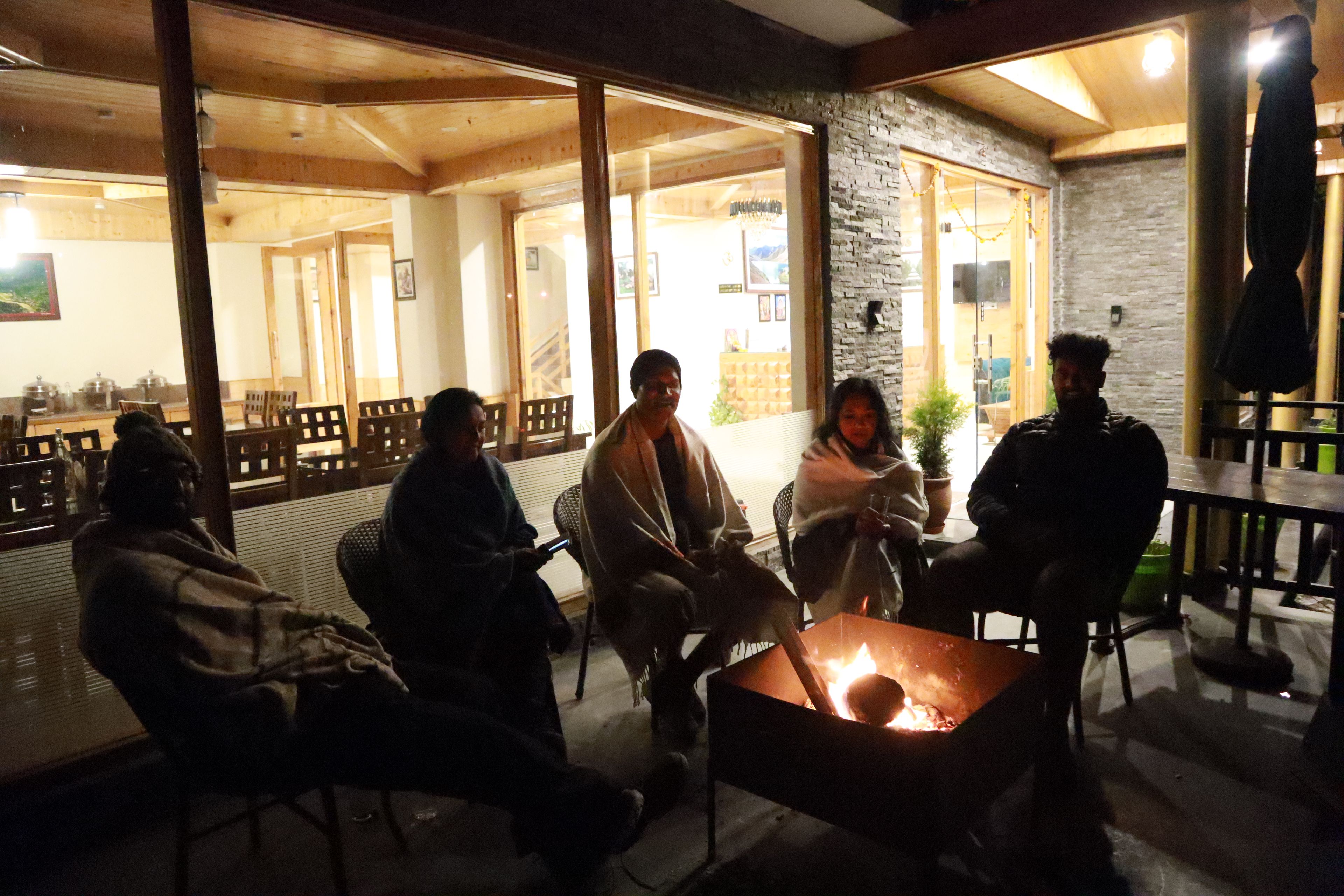 A group of people seated around a table with a lit fire in a room with wooden furniture and stone walls.