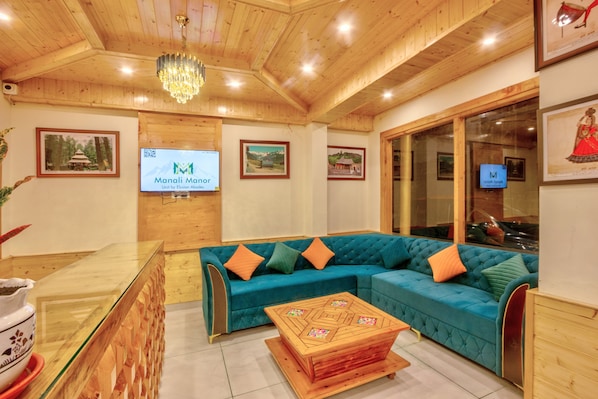A modern living room with a teal sectional sofa, wooden flooring, and a chandelier.