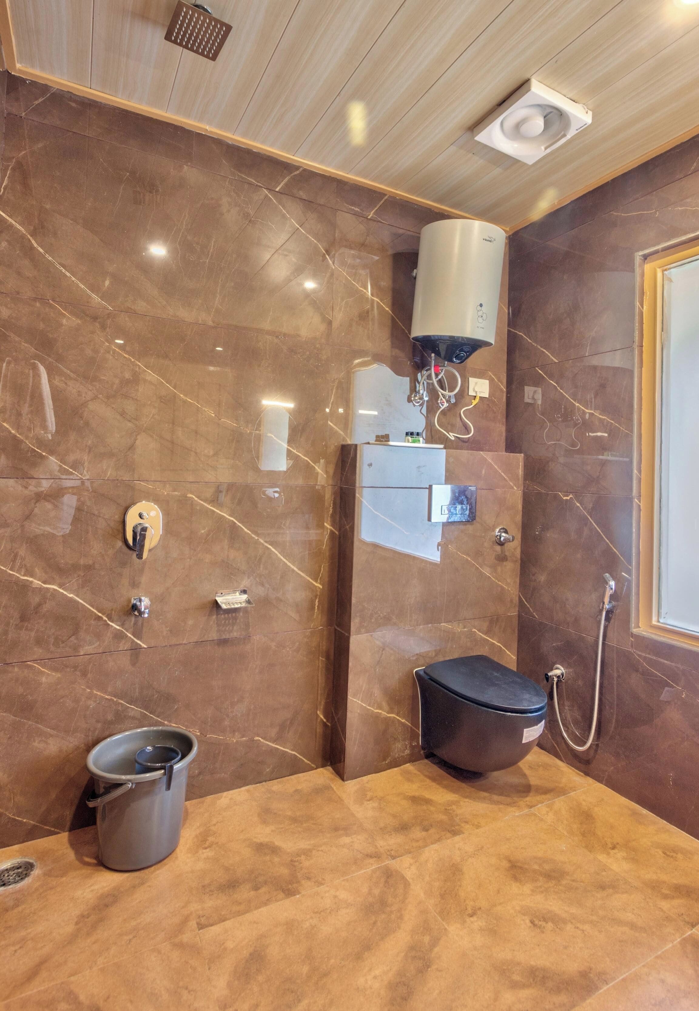 A modern bathroom with a marble wall, a shower area, a black seat, and a bucket.