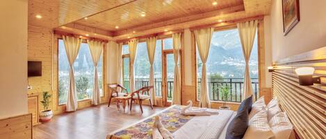 A wooden cabin bedroom with a bed, curtains, a chair, and a view of the mountains.