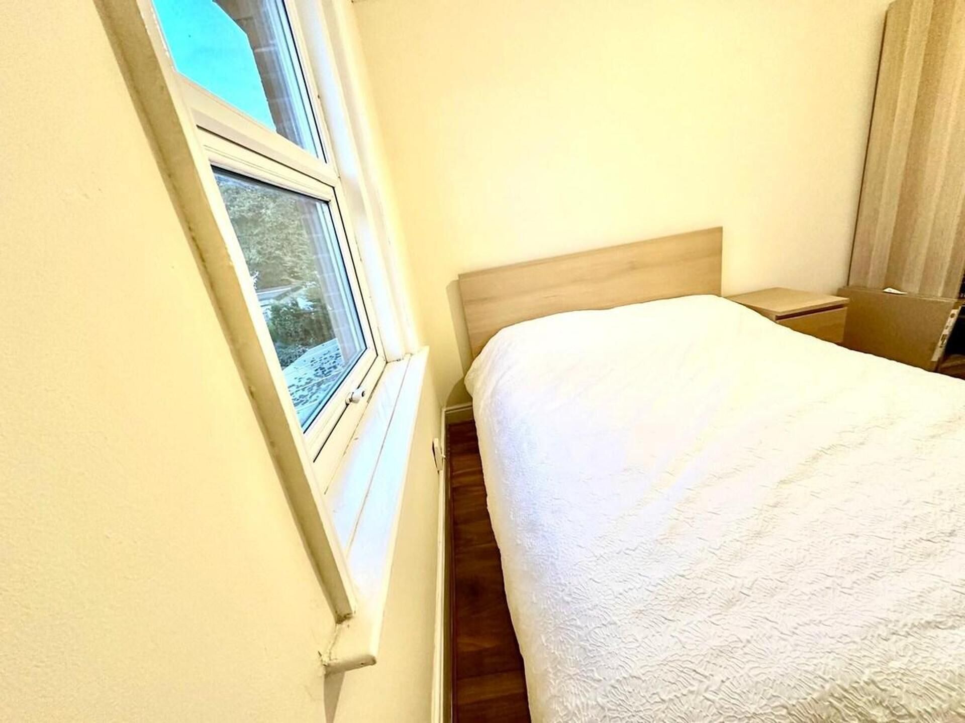 Une chambre à coucher avec un lit, une table de chevet, une fenêtre donnant sur l’extérieur et une tête de lit en bois.