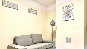 Ένα σαλόνι με έναν γκρι καναπέ, ένα φωτιστικό δαπέδου και διακοσμητικά στοιχεία στους τοίχους με σχέδια.