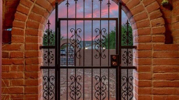 A wrought iron gate with intricate designs, set within a brick archway.