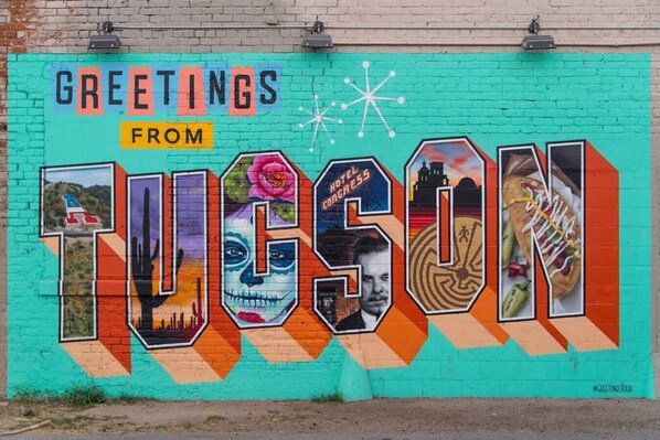Un mural colorido con la palabra 'Tucson' y diversas imágenes, incluyendo un cactus, un hotel y un chile.