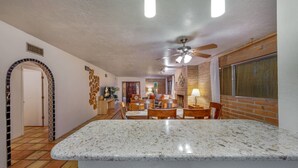 A kitchen with a granite countertop, wooden chairs, and a ceiling fan.