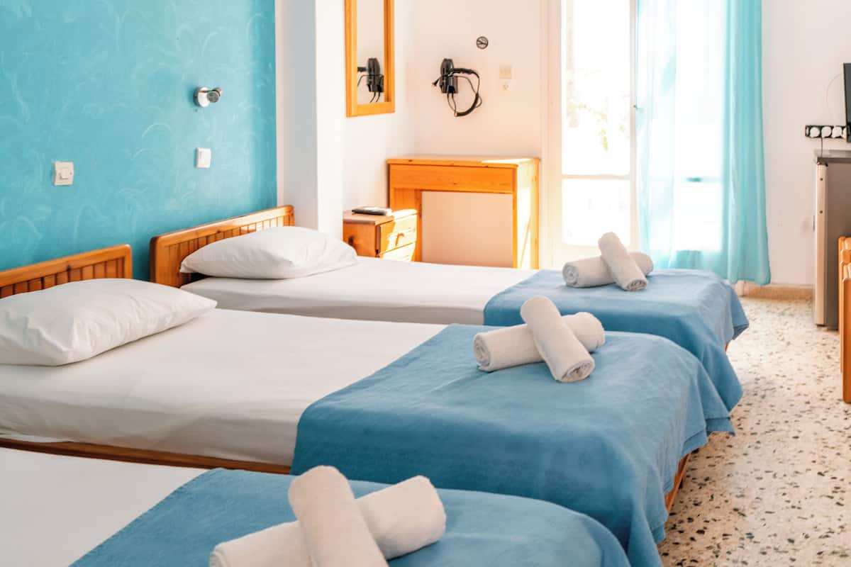A hotel room with three beds, a wooden headboard, a desk, and a window with curtains.