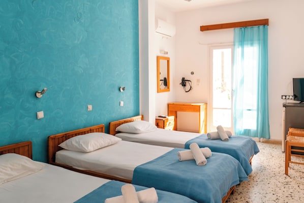 A hotel room with three beds, a desk, a chair, a TV, and a window with curtains. - Dilino Hotel (Santorini)