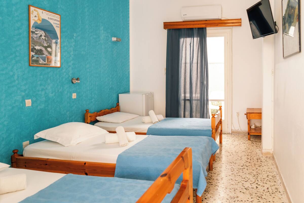 A hotel room with two beds, a TV, a window with curtains, and a poster on the wall.