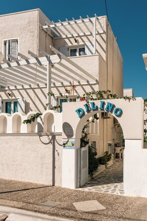 A building with a white facade, a sign reading 'DELINO,' and a covered entrance with a stone pathway leading inside.