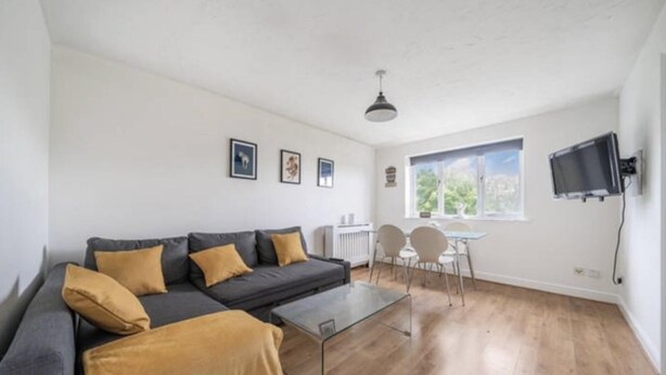 Ein modernes Wohnzimmer mit grauem Sofa, einem Glastisch und einem Essbereich mit kleinem Tisch und Stühlen.