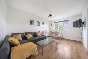 Ein modernes Wohnzimmer mit grauem Sofa, einem Glastisch und einem Essbereich mit kleinem Tisch und Stühlen.