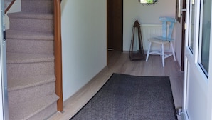Un escalier avec une rampe en bois mène à un palier. Un miroir est accroché au mur, au-dessus d’une porte.