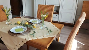 Une table à manger dressée avec des assiettes, des couverts et des verres, entourée de chaises en osier.