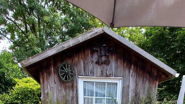Une cabane en bois rustique, dotée d’une fenêtre et d’une roue, est entourée d’une table sur laquelle se trouvent divers ustensiles de cuisine et un vase rempli de fleurs.