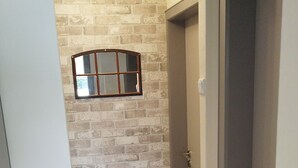 Un couloir étroit avec un mur en briques et un plancher en bois, qui mène à une porte dotée d’une poignée en métal.