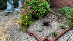 Un jardin avec un mur en briques, une clôture en bois et un chemin de gravier.