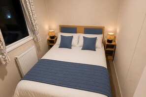 Una cama pequeña y bien hecha con un edredón azul, dos almohadas a juego y dos lámparas de noche.