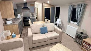 A compact living space with a kitchenette, a sofa, a dining table, and a radiator. - Caravan-blackpool-familyfriendly-activities (Fleetwood)