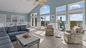 A spacious living area with a large sofa, two armchairs, a coffee table, and a ceiling fan. There are multiple windows offering a view of the ocean. - Hana Kai #173 - Oceanfront Home in the Heart of Surf City! (Surf City)