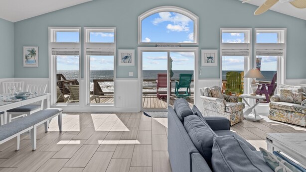 A spacious living room with a view of the ocean, a dining area, and a seating area with colorful chairs. - Hana Kai #173 - Oceanfront Home in the Heart of Surf City! (Surf City)