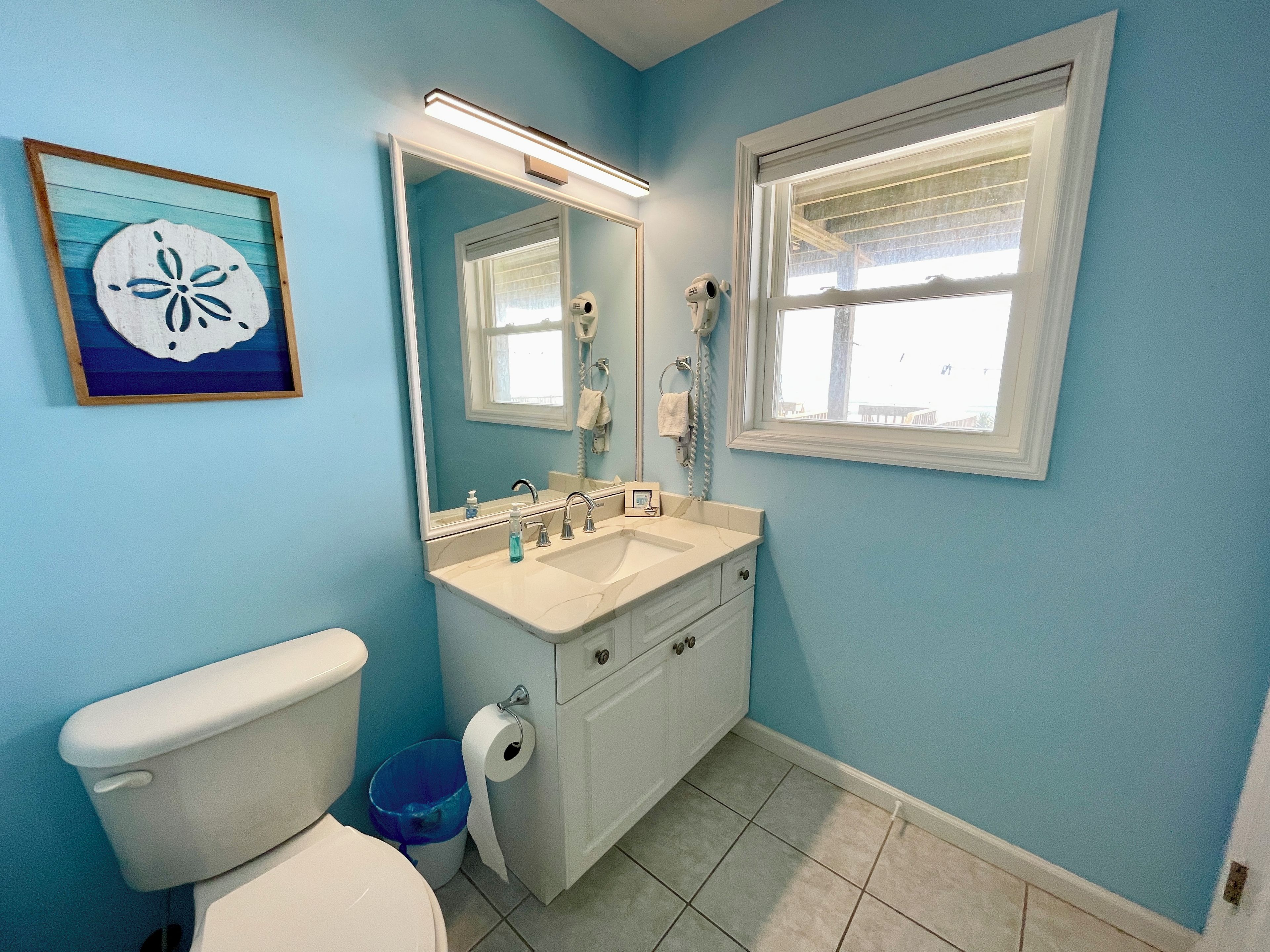 A bathroom with a toilet, sink, mirror, and a window.