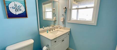 A bathroom with a toilet, sink, mirror, and a window.