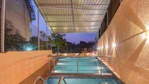 Una piscina interior con zona techada, barandillas metálicas y suelo de baldosas.