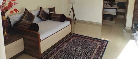 A bedroom with a bed, a floor lamp, a rug, and a vase with flowers.