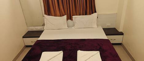 A hotel room with a bed, two pillows, a nightstand, a drawer, and a curtain.