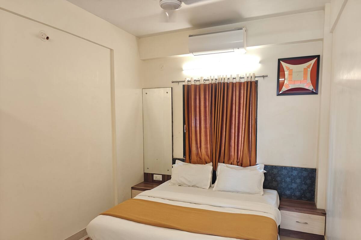 Une chambre à coucher comprenant un lit, une table de chevet, un miroir, un rideau et un climatiseur fixé au mur.