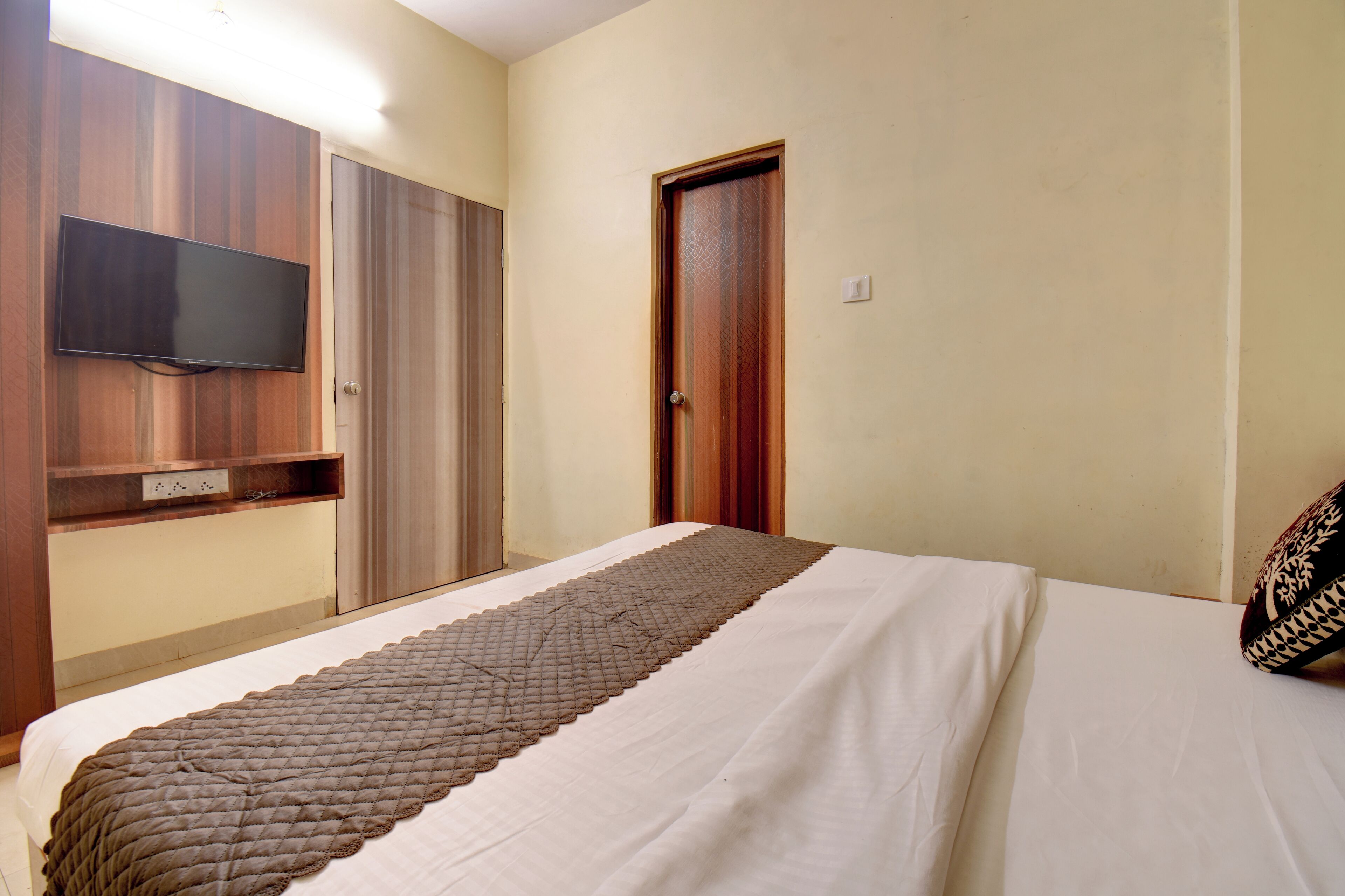 Un dormitorio con una cama, televisión montada en la pared y una puerta.