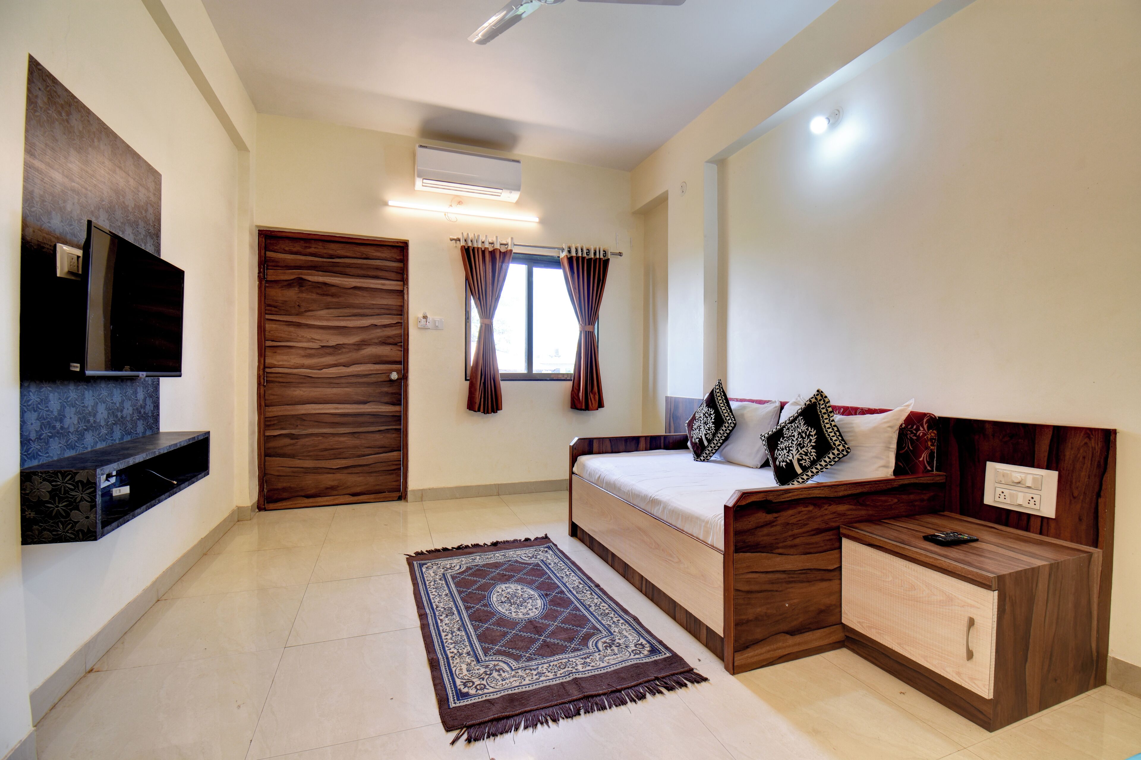 A bedroom with a bed, bedside table, TV, wardrobe, and a window with curtains.