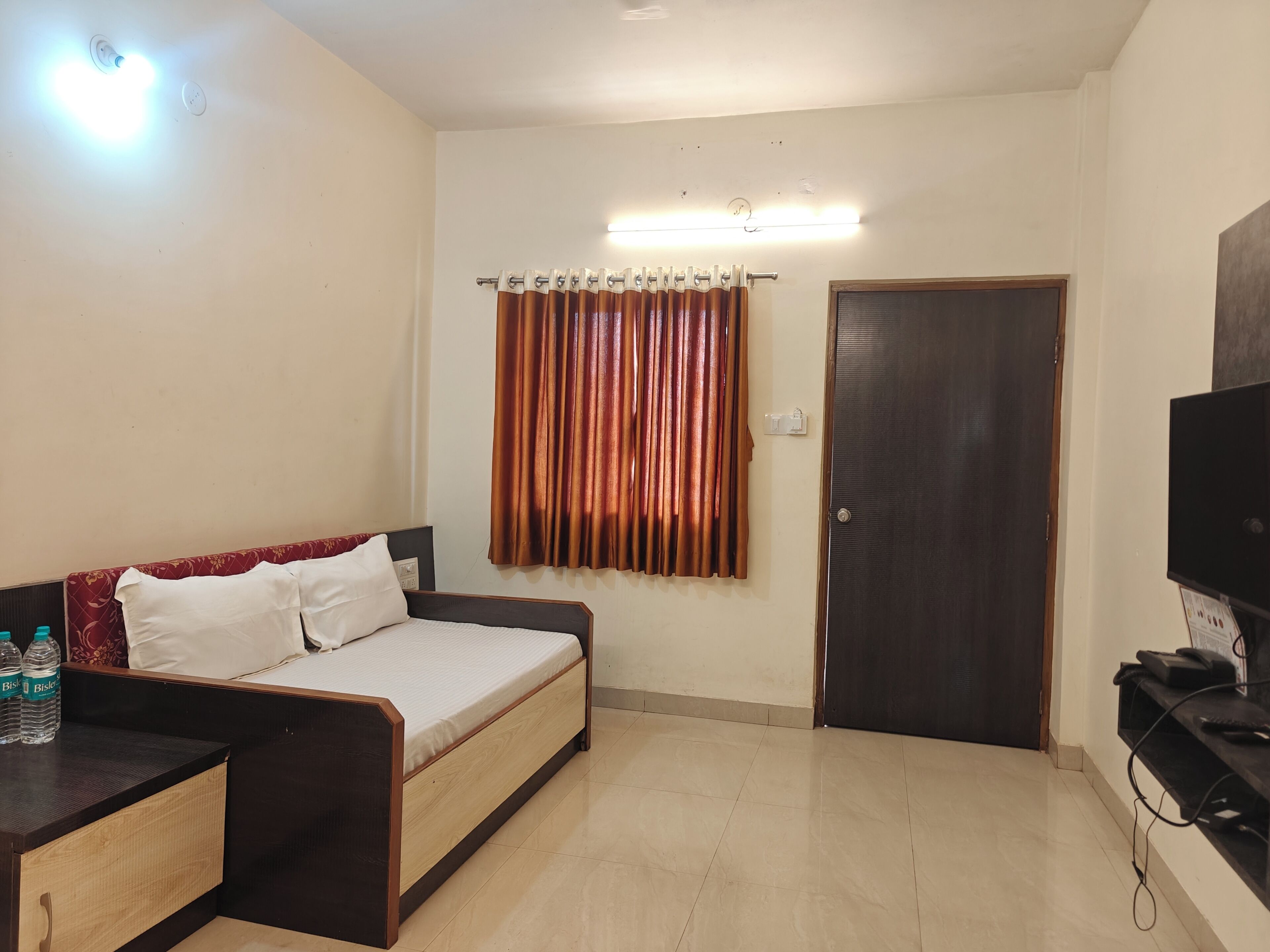 A room with a bed, a desk, a TV, a door, and a curtain.